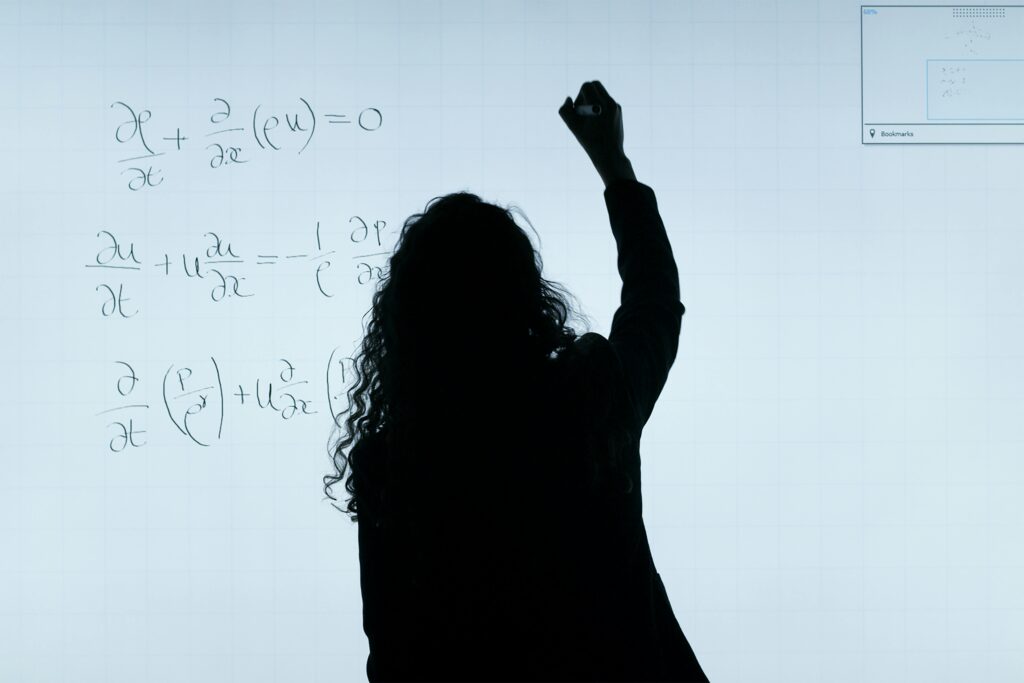 <font dir="auto" style="vertical-align: inherit;"><font dir="auto" style="vertical-align: inherit;">Lar</font></font> A silhouette of a woman writing mathematical equations on a large whiteboard, representing education and analysis.